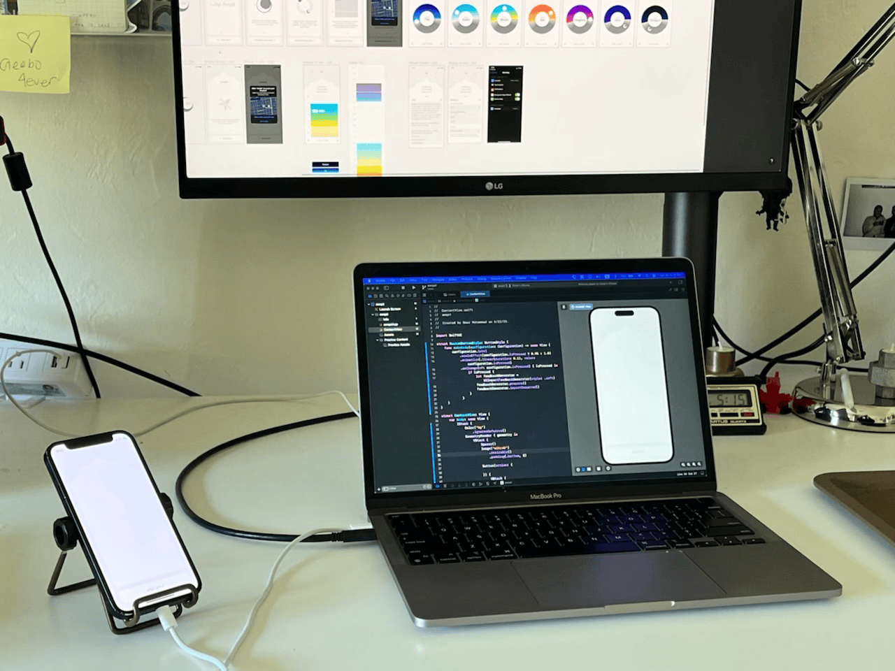 The solo development setup — Xcode with SwiftUI code on the MacBook, the live app running on an iPhone, and the Figma design file visible on an external monitor above.